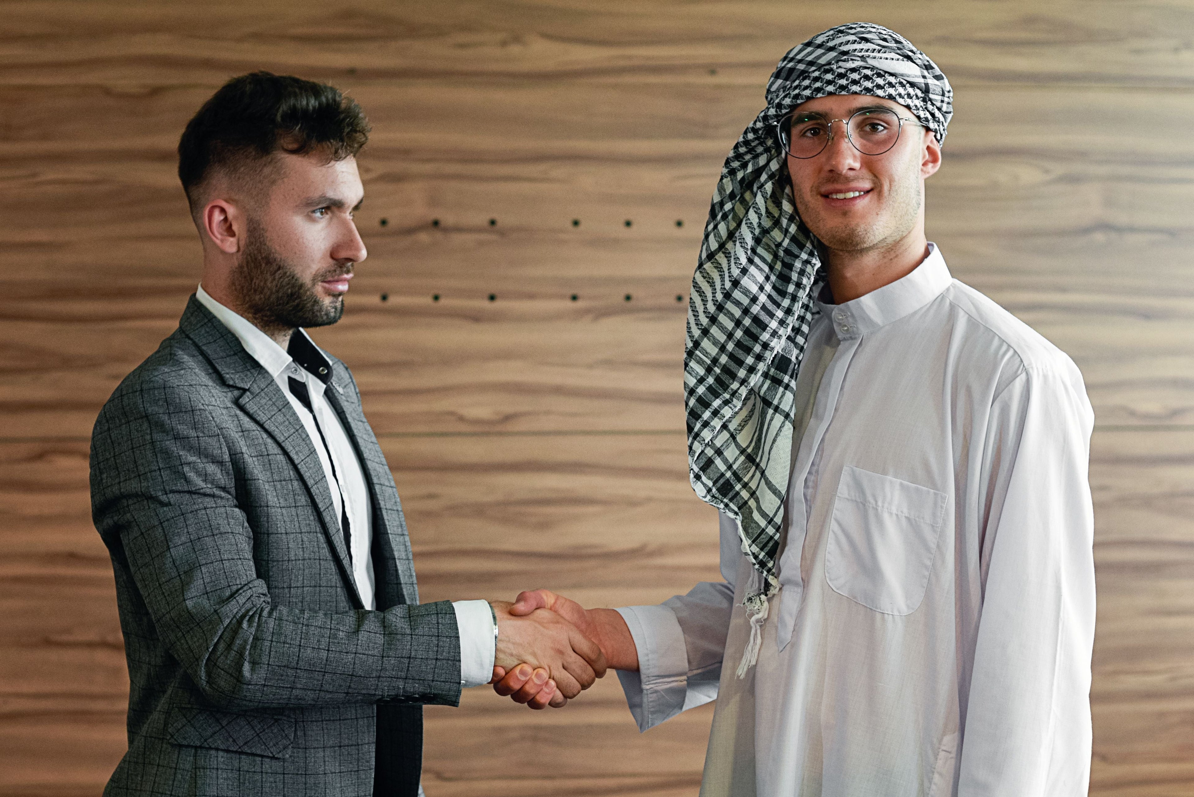 Two businessmen shaking hands, one in traditional Arab attire, finalizing a wholesale deal for Islamic products